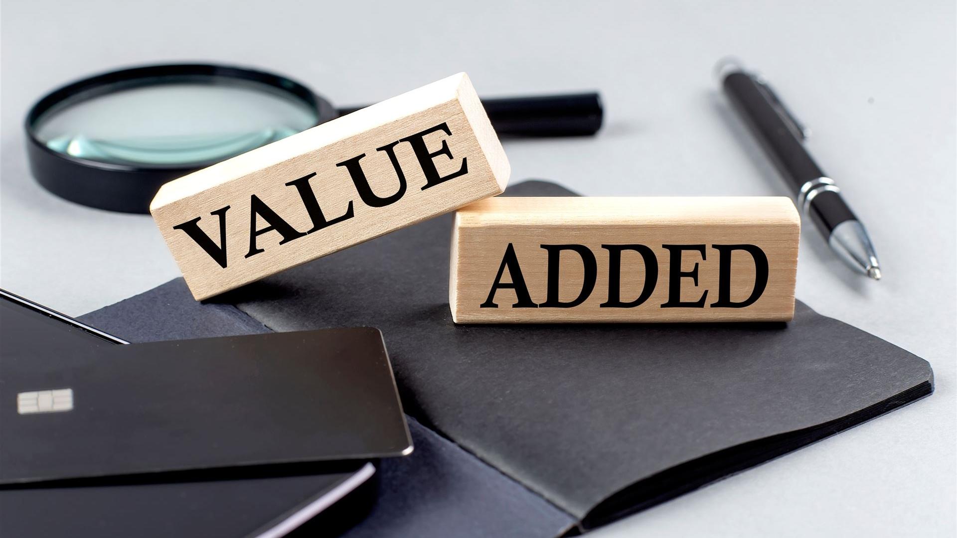 Holzblöcke mit der Aufschrift 'Value Added' auf Schreibtisch mit Notizbuch, Stift und Lupe – symbolisiert den Mehrwert professioneller Beratung durch Kienast Leadership Consulting