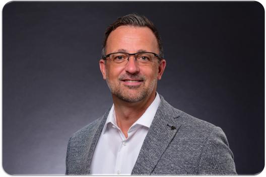 Kai Kienast, Leadership Coach und Berater, im professionellen Business-Portrait mit grauem Sakko und freundlichem Blick vor dunklem Hintergrund