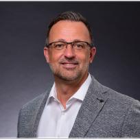 Kai Kienast, Leadership Coach und Berater, im professionellen Business-Portrait mit grauem Sakko und freundlichem Blick vor dunklem Hintergrund