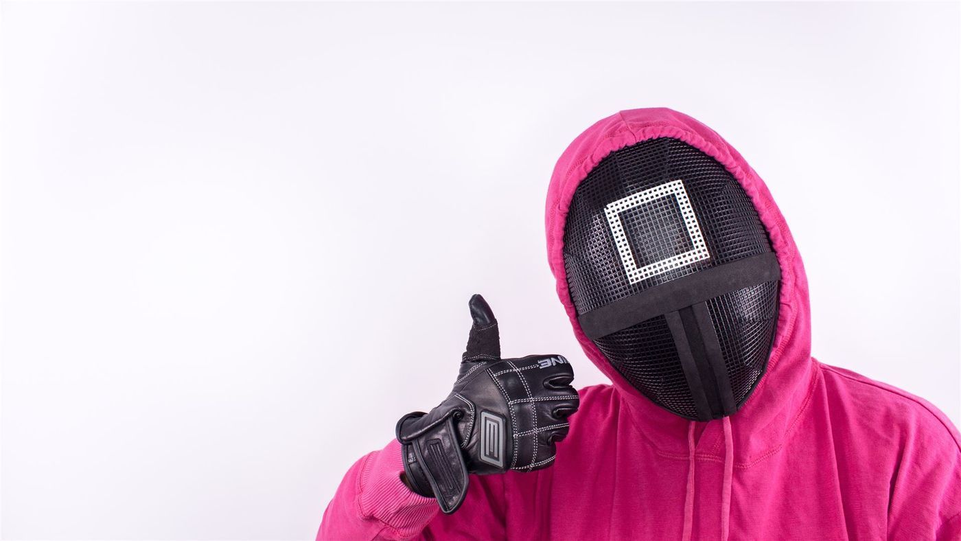 Person im pinkfarbenen Kapuzenanzug mit Maske zeigt den Daumen nach oben